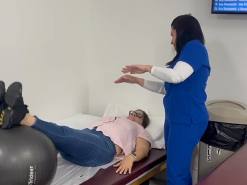 Fisioterapeuta guiando un ejercicio de core y equilibrio con una pelota de estabilidad en All In One Specialty Health